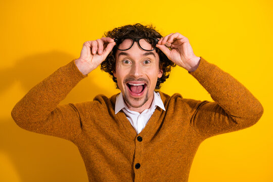 Happy young man in orange cardigan with glasses smiling against a bright yellow background for lively fashion lifestyle and advertising use