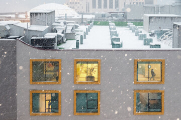 Illuminated windows of a building facade during snowfall