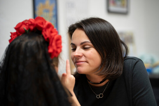 Little girl with a flower wreath on her head showing a thumbs up to her smiling mother indoors. Warm family moment full of love, joy, and connection in Germany.