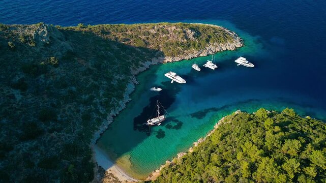 Aerial view of boats sailing on crystal clear turquoise waters surrounded by green hillsides in Mersincik bay, a scenic view, Datca, Mugla, Turkiye.