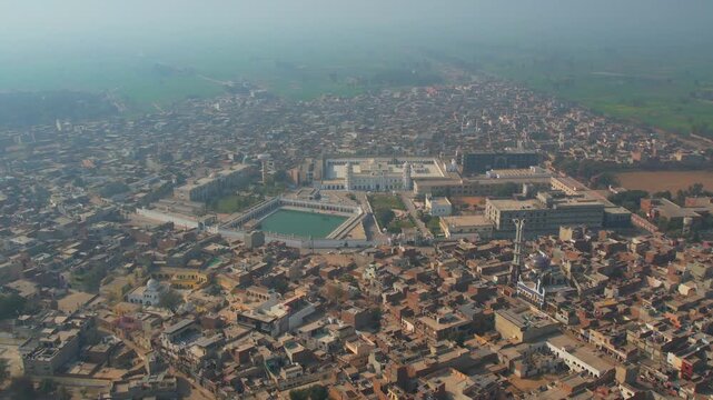 Aerial view of the Gurdwara Janam Asthan, with its rectangular pool reflecting the sky amidst the dense urban landscape, Nankana Sahib, Punjab, Pakistan.