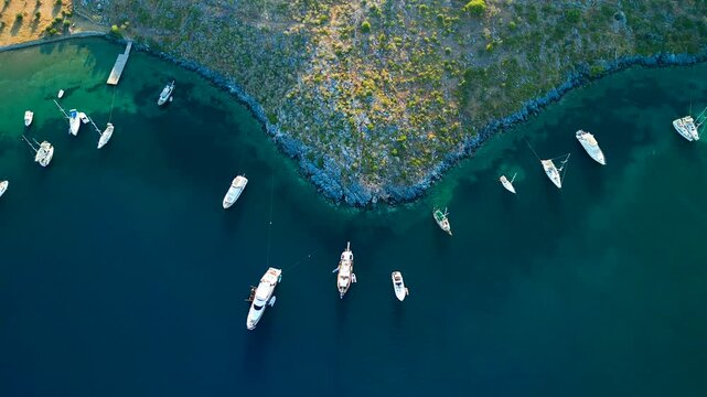 Aerial view of boats scattered on the turquoise sea contrasting the green hillside in the Cokertme bay, Cokertme, Mugla, Turkiye.