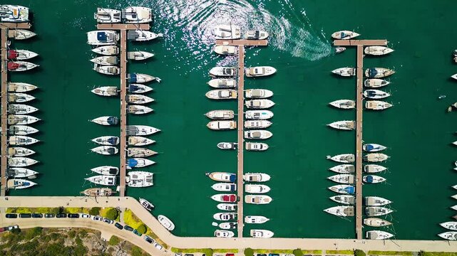 Aerial view of Oren Marina, showcasing rows of boats docked in the turquoise water, a vibrant contrast to the dark vehicles parked along the shore, Oren, Mugla, Turkiye.
