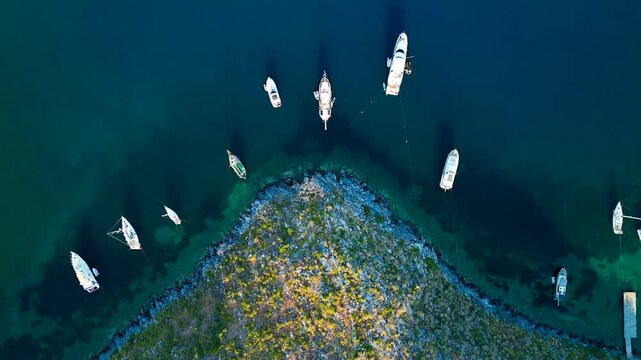 Aerial view of boats sailing near a rugged coastline with vibrant green vegetation meeting the clear turquoise waters of the sea, Cokertme, Mugla, Turkiye.