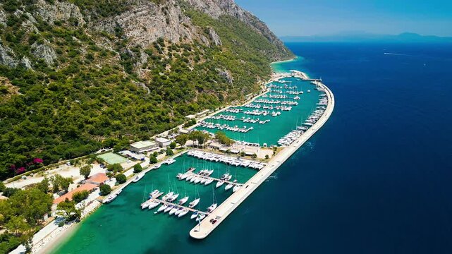 Aerial view of boats docked at Oren Marina, a vibrant scene contrasting emerald waters with the stark white hulls, nestled against a lush mountain, Oren, Mugla, Turkiye.