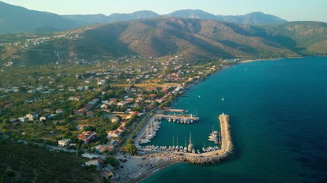 Aerial view of Palamutbuku's turquoise coastline contrasting with the terracotta rooftops nestled against the backdrop of rugged, sun-kissed mountains, Turkiye.
