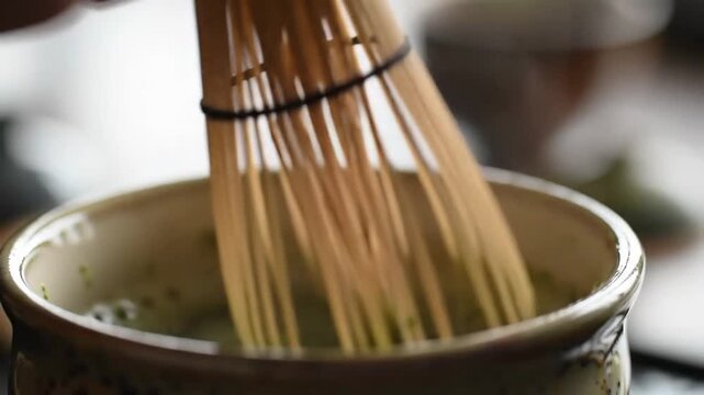 Whisking matcha tea in bowl with bamboo tool. In kitchen, for healthy lifestyle drinks