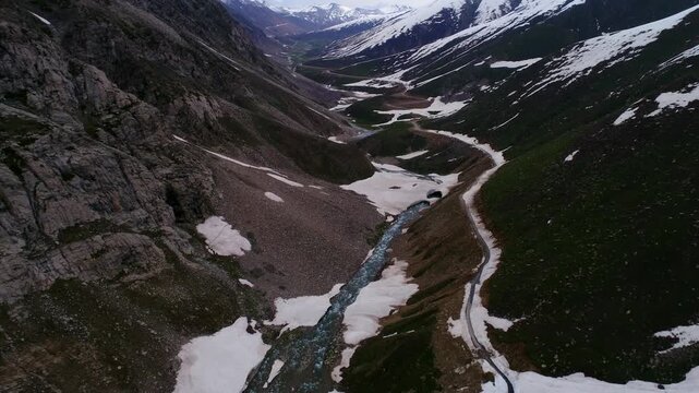 Aerial view of a valley carved by a river, revealing the stark contrast between the rocky terrain and the snowy peaks, Naran, Khyber Pakhtunkhwa, Pakistan.