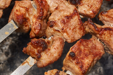 Large pieces of pork being grilled on skewers over hot charcoal. Delicious barbecue with a golden crust cooking outdoors during a picnic or countryside gathering.