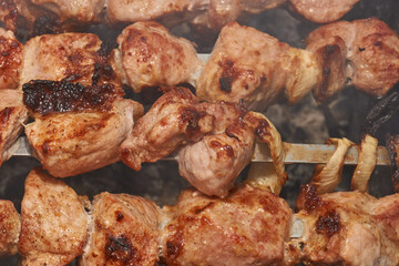 Large pieces of pork being grilled on skewers over hot charcoal. Delicious barbecue with a golden crust cooking outdoors during a picnic or countryside gathering.