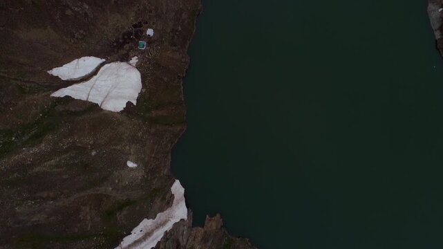 Aerial view of Lulusar Lake, where dark waters meet rugged terrain and patches of white snow, creating a contrast of textures, Naran, Khyber Pakhtunkhwa, Pakistan.