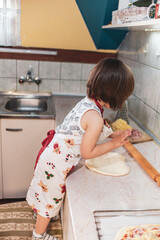 A little girl is making pizza with dough and different ingredients
