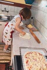 A little girl is making pizza with dough and different ingredients
