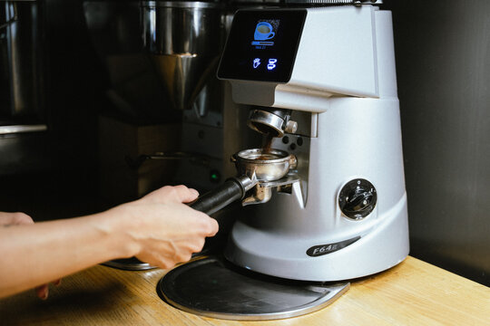 A barista prepares freshly ground coffee in a modern espresso machine.