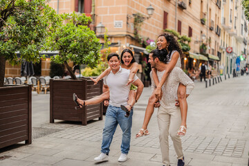 Young adults laughing and playing piggyback ride on city street