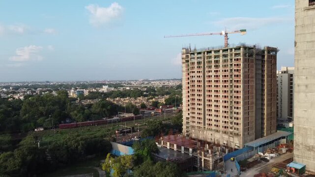 Kishan Ganj, India - 31 July 2025: Aerial view of buildings under construction, train on the tracks, and a crane against the backdrop of a clear sky.