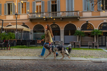 Young woman walking a dog on a leash along a european city street
