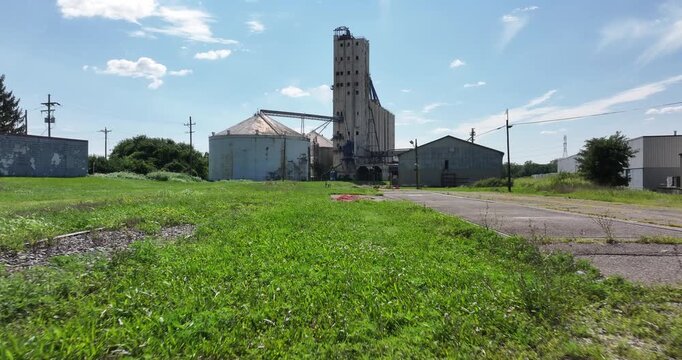 Cincinnati, United States - 02 August 2025: Aerial view of weathered grain elevators stand tall against the skyline, framed by vibrant green grass and a clear blue sky.