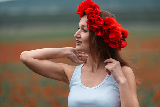 Woman poppy flower crown stands in vast field of blooming red flowers