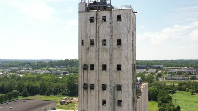 Cincinnati, United States - 02 August 2025: Aerial view of a weathered white tower block rising against a backdrop of lush greenery and urban development.