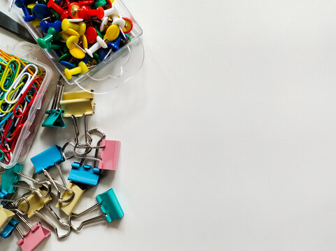 Assorted office supplies on a white background include colorful push pins, binder clips, and paper clips. 