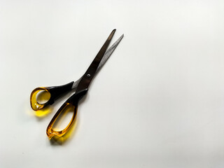 Metal scissors with sharp, pointed blades and translucent yellow plastic handles rest on a plain white surface. 