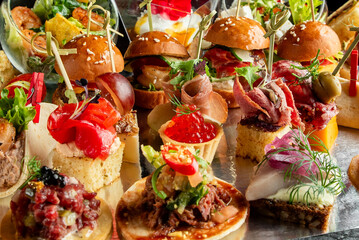 A close-up, high-angle view of an elegant, vibrant assortment of gourmet mini appetizers, including sliders, canapés, and tartlets, at a catering buffet