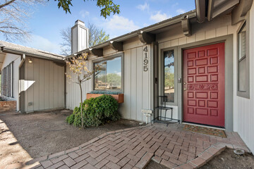 The front exterior of a house featuring a red door and a brick walkway