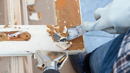 Carpenter using heat gun and wood scraper removes paint from old wooden window. Construction industry, carpentry. Restoration. 