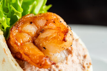 A close-up shot of a seasoned, cooked shrimp resting on a light brown spread and lettuce in a tortilla wrap, ideal for food photography and culinary blogs.