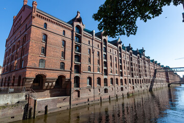 Classic view of the historic Speicherstadt warehouse district in Hamburg, featuring red brick facades reflected in the waters of the canal under a clear blue sky