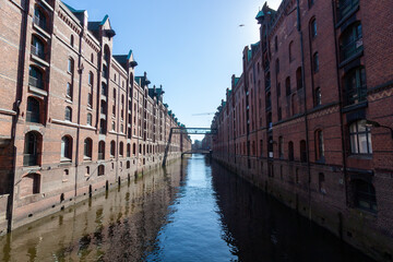 Classic view of the historic Speicherstadt warehouse district in Hamburg, featuring red brick facades reflected in the waters of the canal under a clear blue sky