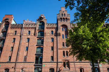 The impressive red brick facade of a traditional warehouse in Hamburg's Speicherstadt, housing Miniatur Wunderland and a Digital Hub, under a bright blue sky