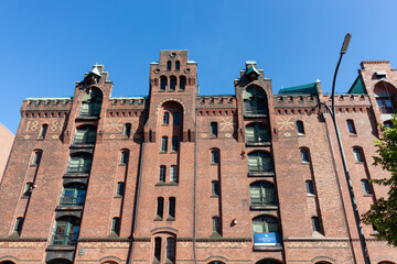 The impressive red brick facade of a traditional warehouse in Hamburg's Speicherstadt, housing Miniatur Wunderland and a Digital Hub, under a bright blue sky