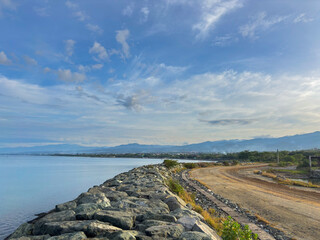 Beautiful coastal landscape with calm waters and mountains under a cloudy blue sky perfect for travel inspiration