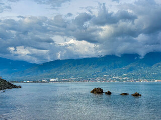 Dramatic clouds hover over tranquil blue water and mountains, a peaceful palu city beckons in the distance