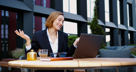 Handsome woman using laptop having an online meeting with client or business partner during lunch break of the cafe. Smiling mature successful businesswoman communicates remotely on a video call near