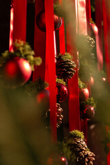 A festive Christmas decoration with red ribbons, pinecones, and shiny ornaments, warmly lit by sunlight to create a natural and cozy holiday atmosphere.