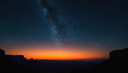 Desert canyon landscape at dusk displays vibrant orange sunset on distant horizon. Dark night sky above countless bright stars, Milky Way galaxy. Dramatic rock formations silhouette against glowing