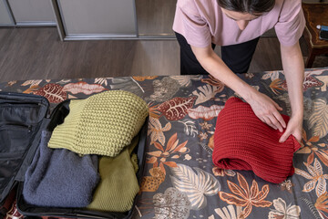 Fototapeta premium Female hands carefully arranging various colorful sweaters for packing into suitcase