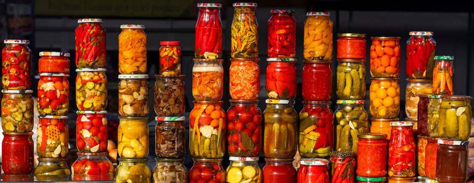 Assorted pickled vegetables in jars on a market stall with bright colors and glass containers - Powered by Adobe