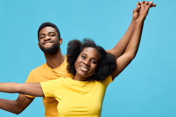 Happy young African American couple enjoying their time together in vibrant yellow and orange t shirts against a bright blue background, expressing joy and connection