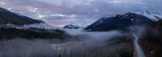Misty Mountain Valley in BC, Canada With Snow-Capped Peaks and Winding Road