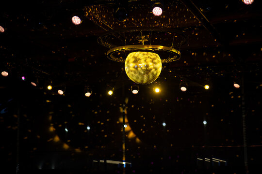 A large yellow disco ball hanging in a modern conference hall, creating a vibrant and stylish atmosphere with reflective lighting effects. The interior features contemporary design elements
