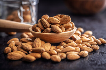 Almond kernel nuts on wooden spoon on black table.