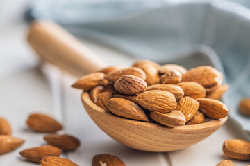 Almond kernel nuts on wooden spoon on white table.