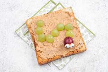 Creative snack idea with peanut butter and grapes shaped like a caterpillar on toasted bread