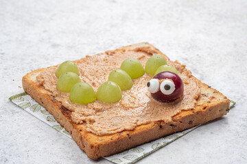 Creative snack idea with peanut butter and grapes shaped like a caterpillar on toasted bread