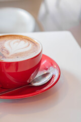 Cup of coffee sprinkled with cinnamon in a red cup on a light background on the left side, vertical frame