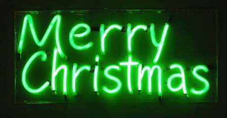 Bright green neon sign displays Merry Christmas. Dark background emphasizes glowing text. Festive holiday illumination. Simple rectangular shape.
